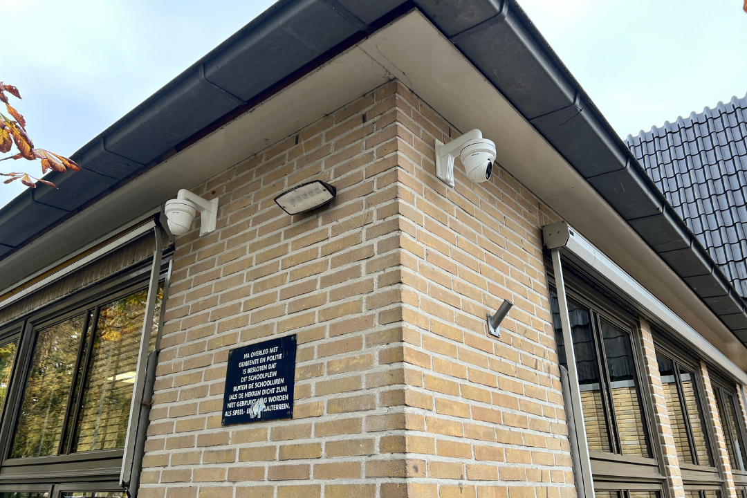 Beveiligingscamera's aan hoek van bakstenen gebouw.