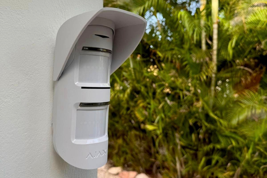 Bewegingsdetector gemonteerd op muur, omgeven door planten.